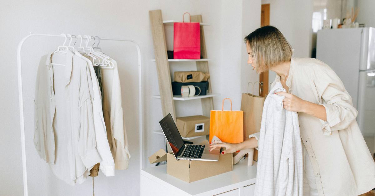 Frau mit Kleidung und Tüten drumherum, beim Online-Shopping am Laptop