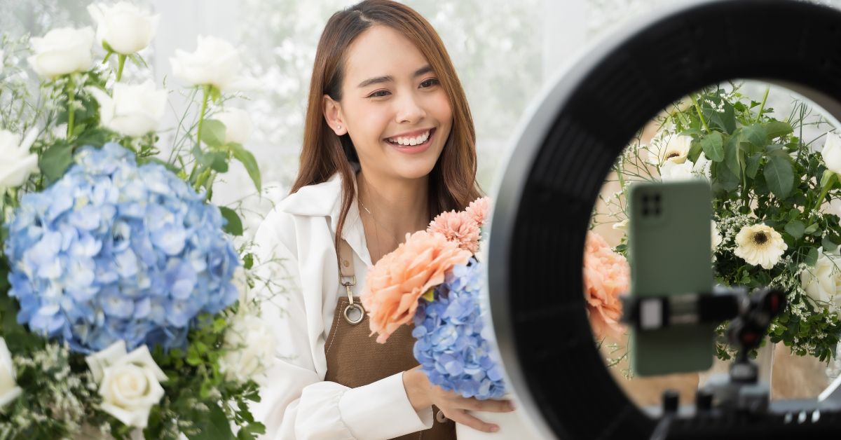 Eine Frau präsentiert Blumen vor einem Ringlicht und einem Smartphone