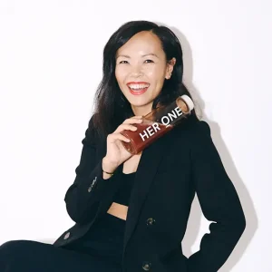 Business-Portr&auml;t von Chanyu Xu in schwarzem Outfit h&auml;lt eine Getr&auml;nkeflasche mit der Aufschrift HER ONE vor wei&szlig;em Hintergrund