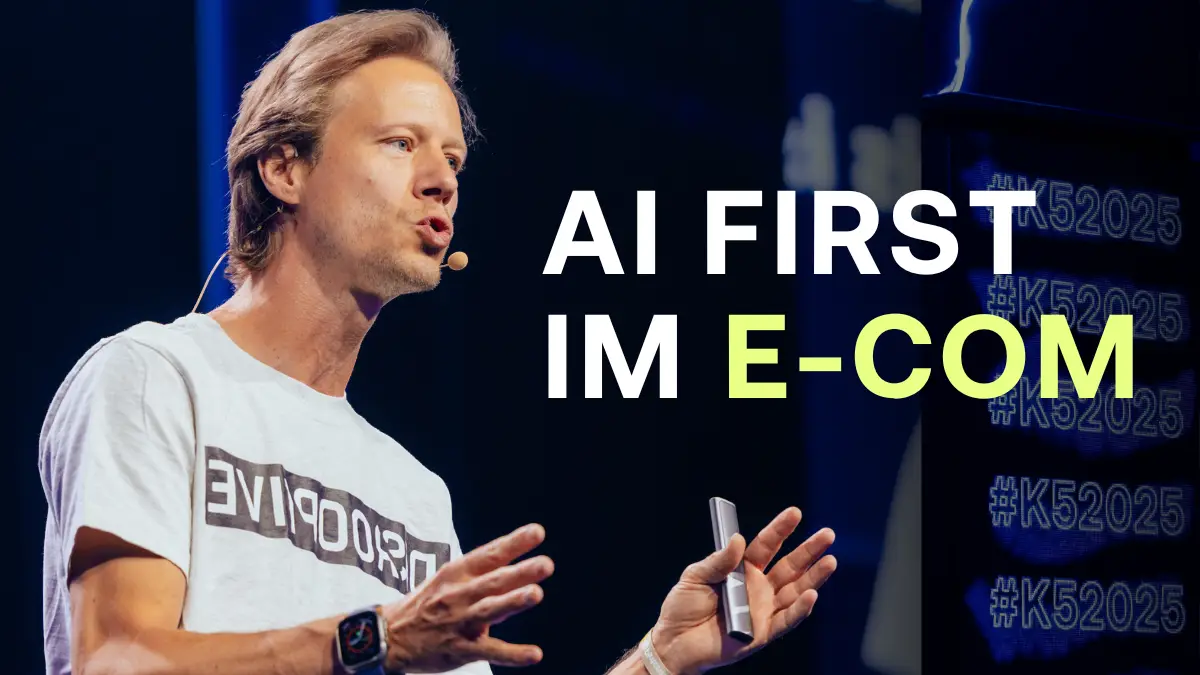 Vortrag auf der K5 Konferenz zum Thema AI First im E-Com. Ruppert Bodmeier spricht auf einer dunklen B&uuml;hne in einem wei&szlig;en T-Shirt mit Mikrofon.