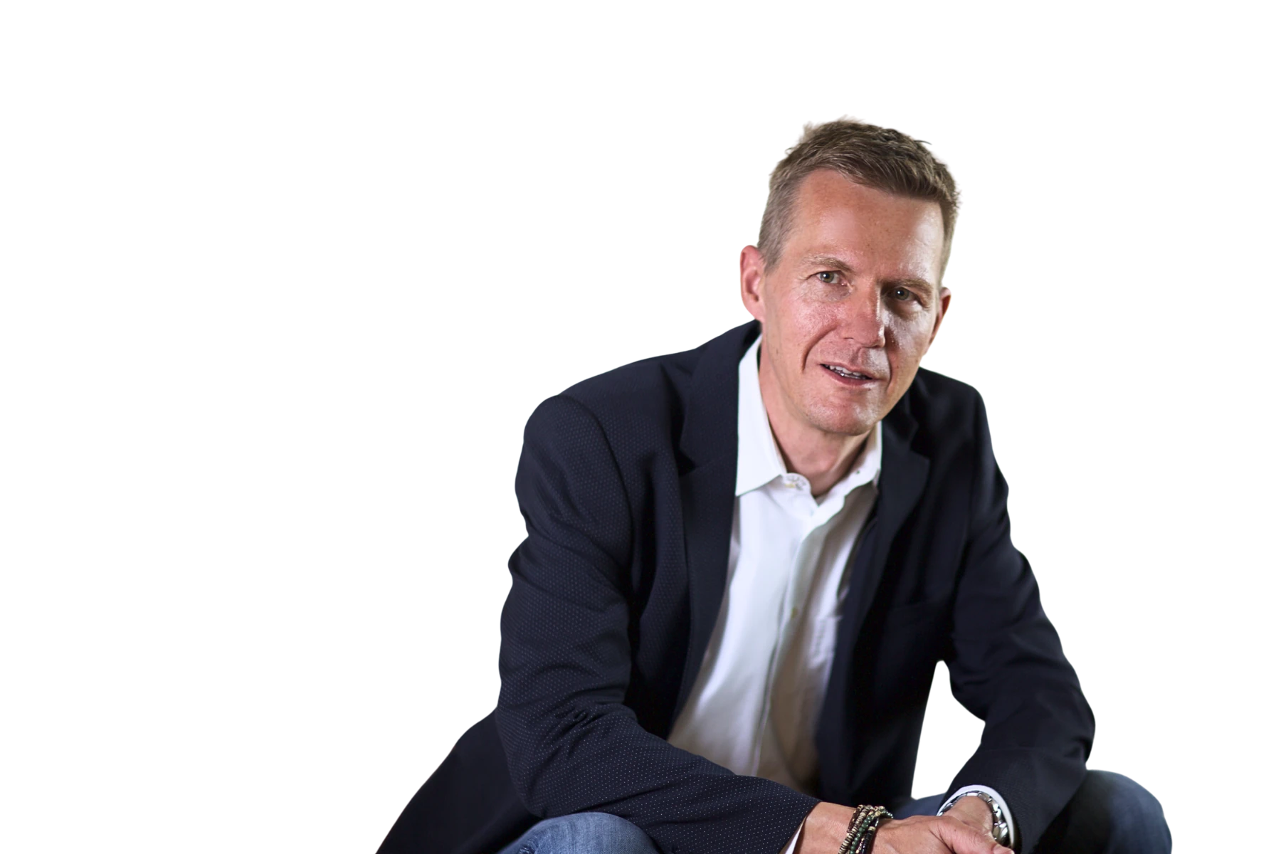 Professionelles Portrait von Stephan Widmer, CEO und Mitgründer der Beliani Group, mit kurzen braunen Haaren in dunklem strukturiertem Sakko und weißem Hemd vor weißem Hintergrund, sitzend und freundlich lächelnd in die Kamera blickend.