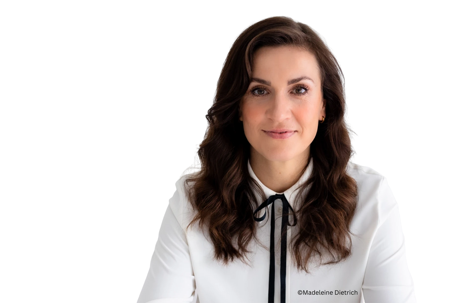K5 Female in Retail Podcast Freigestelltes Porträt von Magdalena Rogl: Sie blickt lächelnd in die Kamera, hat lange wellige braune Haare und trägt eine weiße Bluse mit schwarzer Schleife am Kragen. Unten rechts im Bild steht der Copyright-Hinweis „©Madeleine Dietrich“.