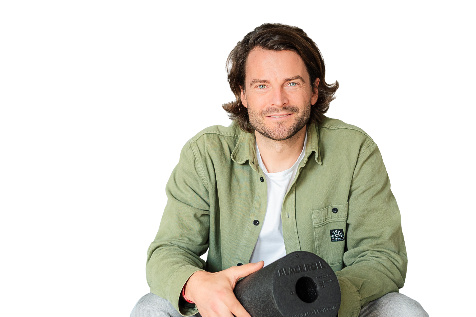 Freisteller von Marius Keckeisen, Chief Innovation Officer und Mitgründer von BLACKROLL, im grünen Hemd und weißem T-Shirt vor schwarzem Hintergrund. Er lächelt in die Kamera und hält eine BLACKROLL-Faszienrolle – Protagonist der ChefTreff Podcast-Episode über Regeneration, Innovation und die Entwicklung einer globalen Gesundheitsmarke.