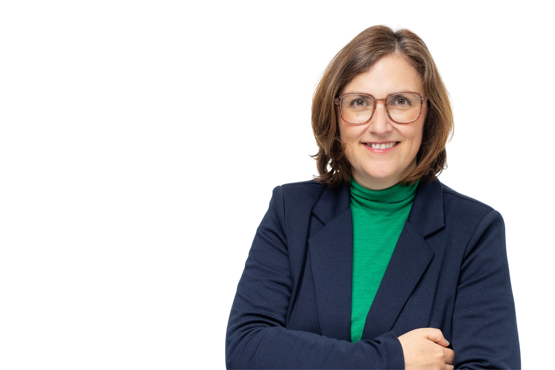 Professionelles Portrait von Nicole Wienigk, Lead Sales bei REWE Group Retail Media Connect, mit braunen schulterlangen Haaren und Brille in grünem Rollkragenpullover und dunklem Blazer vor weißem Hintergrund, freundlich lächelnd mit verschränkten Armen.