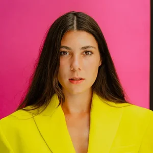 Portr&auml;t von Anastasia Barner mit langen dunklen Haaren im leuchtend gelben Blazer vor pinkem Hintergrund, modernes Business- und Fashion-Portr&auml;t f&uuml;r Personal Branding und Medienauftritte