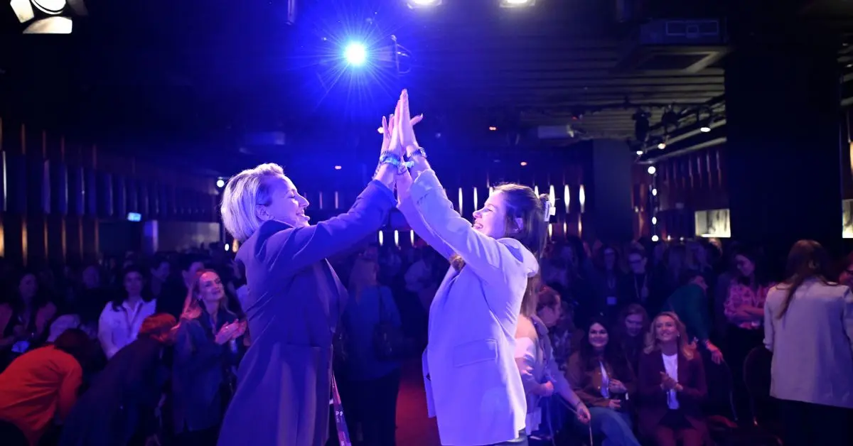 Verena Lindner und Verena Schl&uuml;pmann auf der B&uuml;hne des K5 Female Circle Events geben sich ein High Five, vor ihnen ein applaudierendes Publikum im Eventsaal.