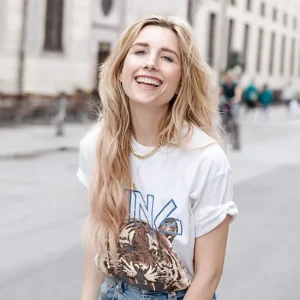 Martina Panchyrz mit langen blonden Haaren tr&auml;gt wei&szlig;es T-Shirt mit Print und Jeans, urbanes Streetstyle-Portr&auml;t im Freien vor Stadtkulisse
