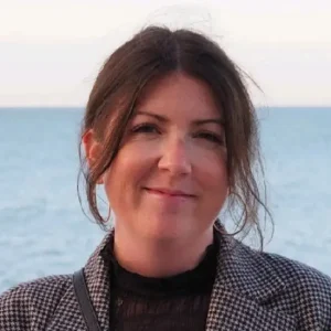 Portr&auml;t von Martina Ponath mit dunklem Haar vor dem Meer, tr&auml;gt gemusterten Blazer und schwarzes Oberteil