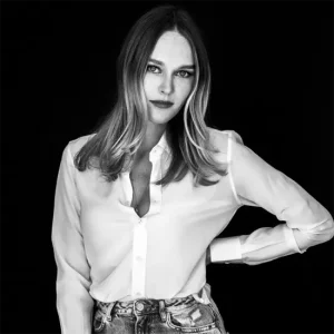 Schwarz-wei&szlig; Portr&auml;t von Natalie Hanczewski mit schulterlangen Haaren in wei&szlig;er Bluse und Jeans vor schwarzem Hintergrund