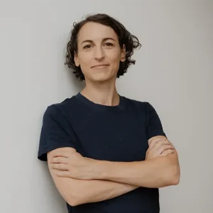 Selbstbewusste Natascha Wegelin mit kurzen lockigen Haaren im dunkelblauen T-Shirt, Arme verschr&auml;nkt vor hellem Hintergrund