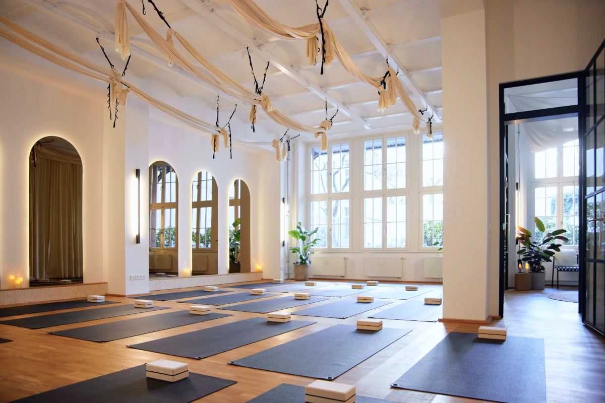 Heller Yoga-Studioraum in Berlin Prenzlauer Berg mit schwarzen Matten, Blöcken, Rundbogen-Spiegeln und hängenden Stoffbahnen.