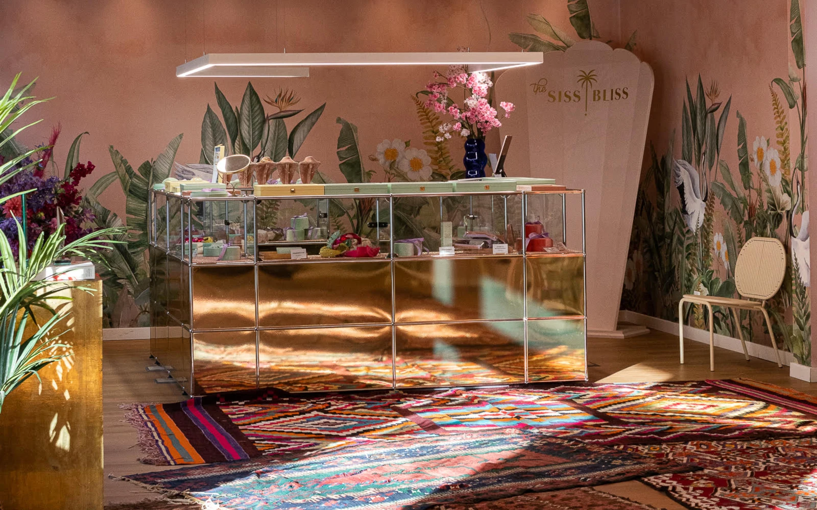 Innenansicht des "The SISS BLISS" Showrooms während des Blissfull Brunch Events. Im Zentrum steht eine goldene Verkaufsvitrine auf bunten Teppichen, umgeben von floraler Tapete mit Flamingo-Motiven und dem Markenlogo.