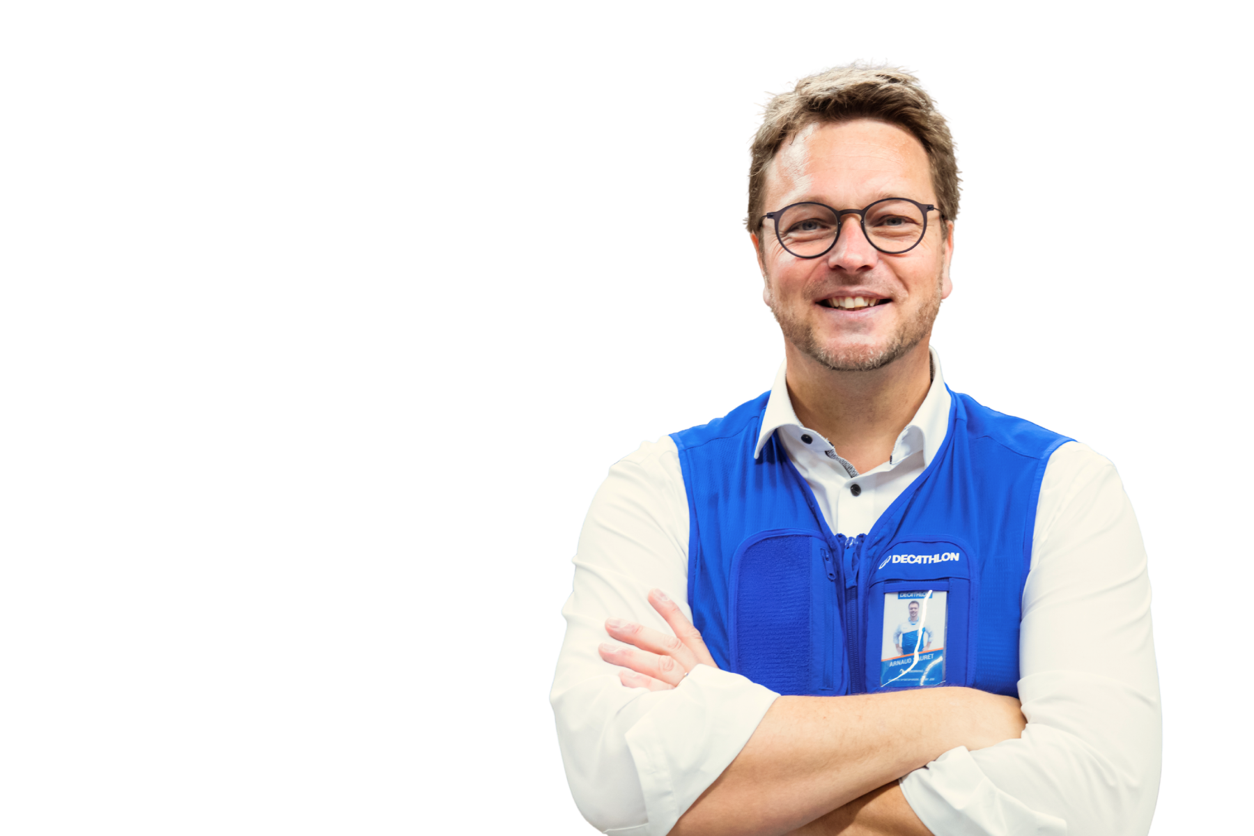 Freigestelltes Porträt von Arnaud Sauret, CEO von Decathlon Deutschland. Er trägt eine Brille und die blaue Decathlon-Weste über einem weißen Hemd, hat die Arme verschränkt und lächelt freundlich in die Kamera.