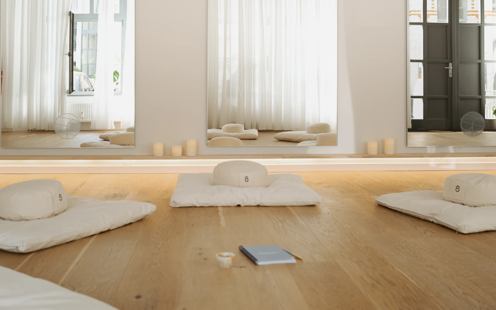 Heller, minimalistischer Raum für die Deep Relaxation Session mit weißen Meditationskissen, Kerzen und Spiegeln auf hellem Holzboden. Ruheoase zur mentalen Vorbereitung vor dem K5 Female Circle Event.