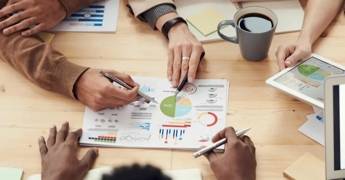 Mehrere Personen analysieren gemeinsam E-Commerce-Kennzahlen und Diagramme mit Charts und Margen auf einem Tisch.