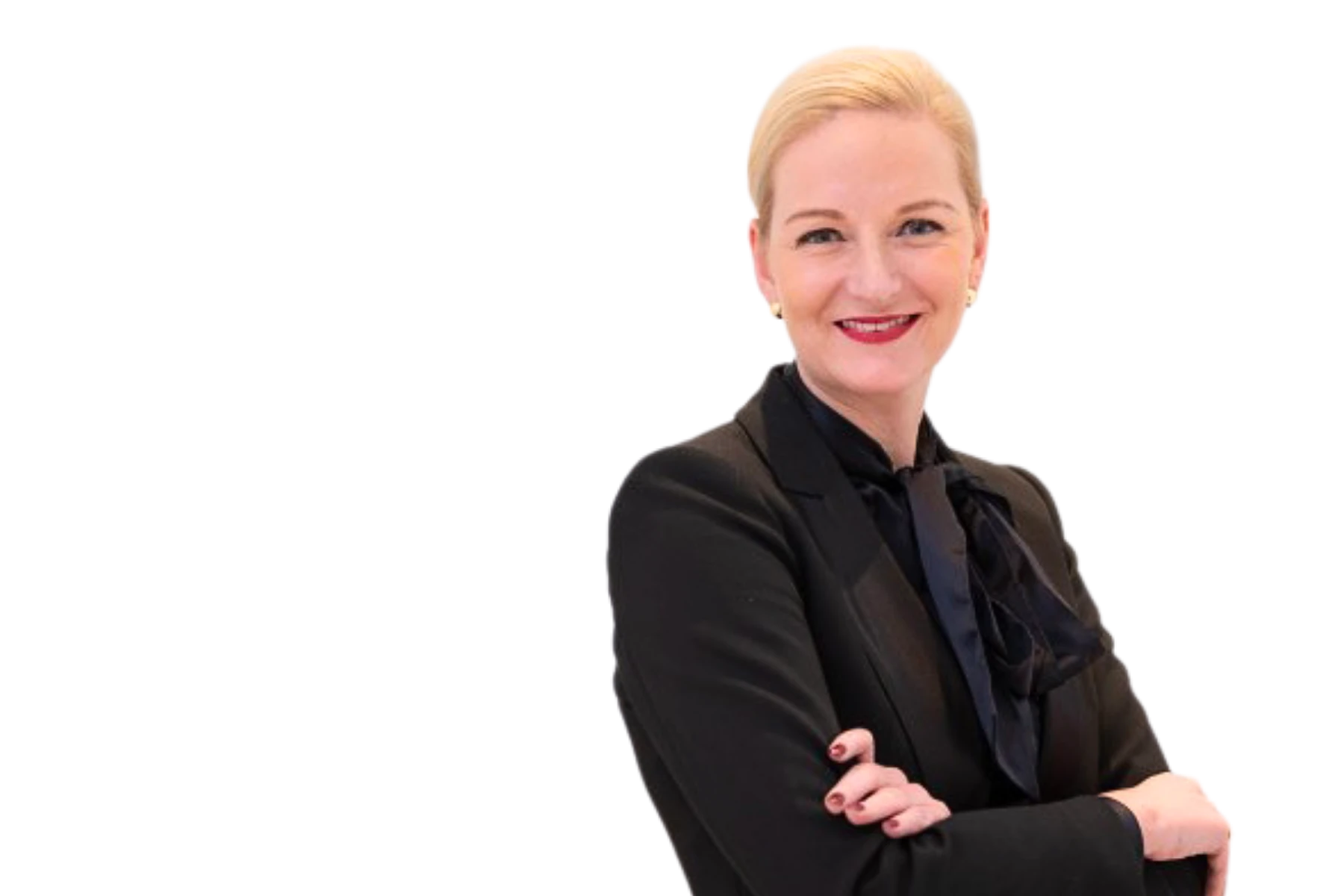 Freigestelltes Porträt von Catharina Christe. Sie trägt einen eleganten schwarzen Blazer mit einer dunklen Schluppenbluse, hat blonde zurückgebundene Haare, die Arme verschränkt und lächelt selbstbewusst in die Kamera. Der Hintergrund ist komplett weiß.