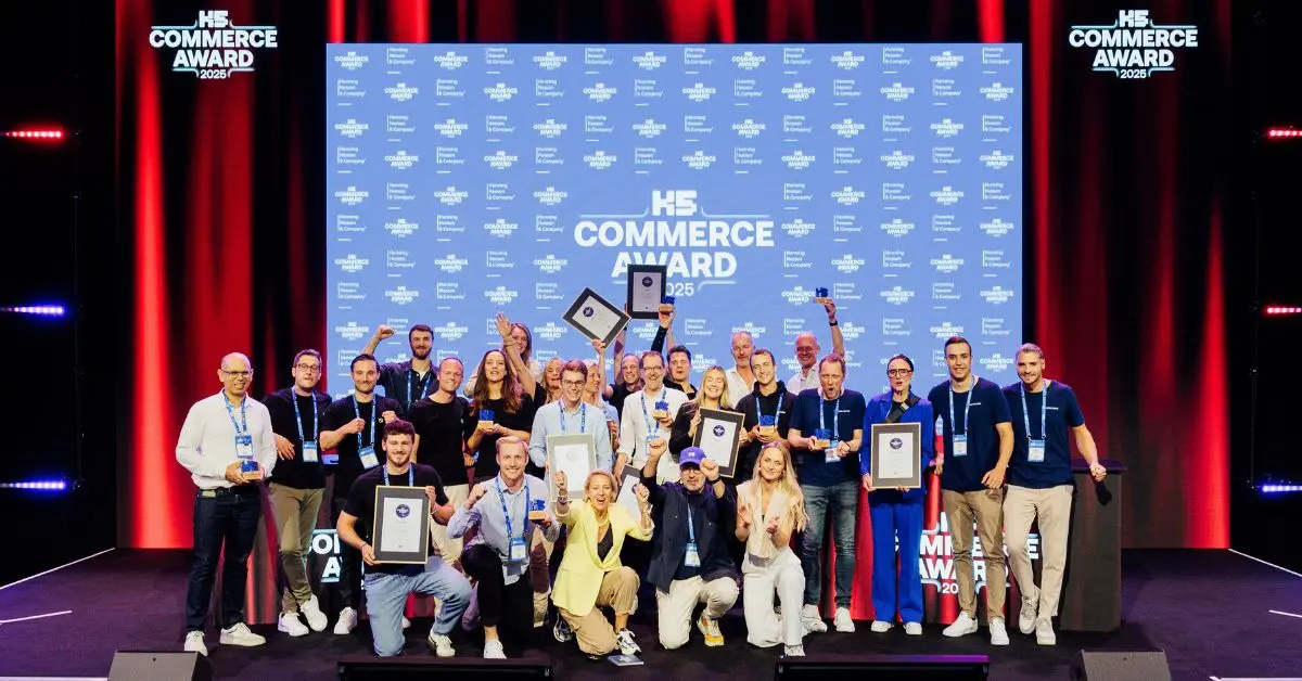 Gruppenfoto der GewinnerInnen des K5 Commerce Award auf einer B&uuml;hne mit rotem Licht, Pokalen und Urkunden vor gro&szlig;em K5-Backdrop.