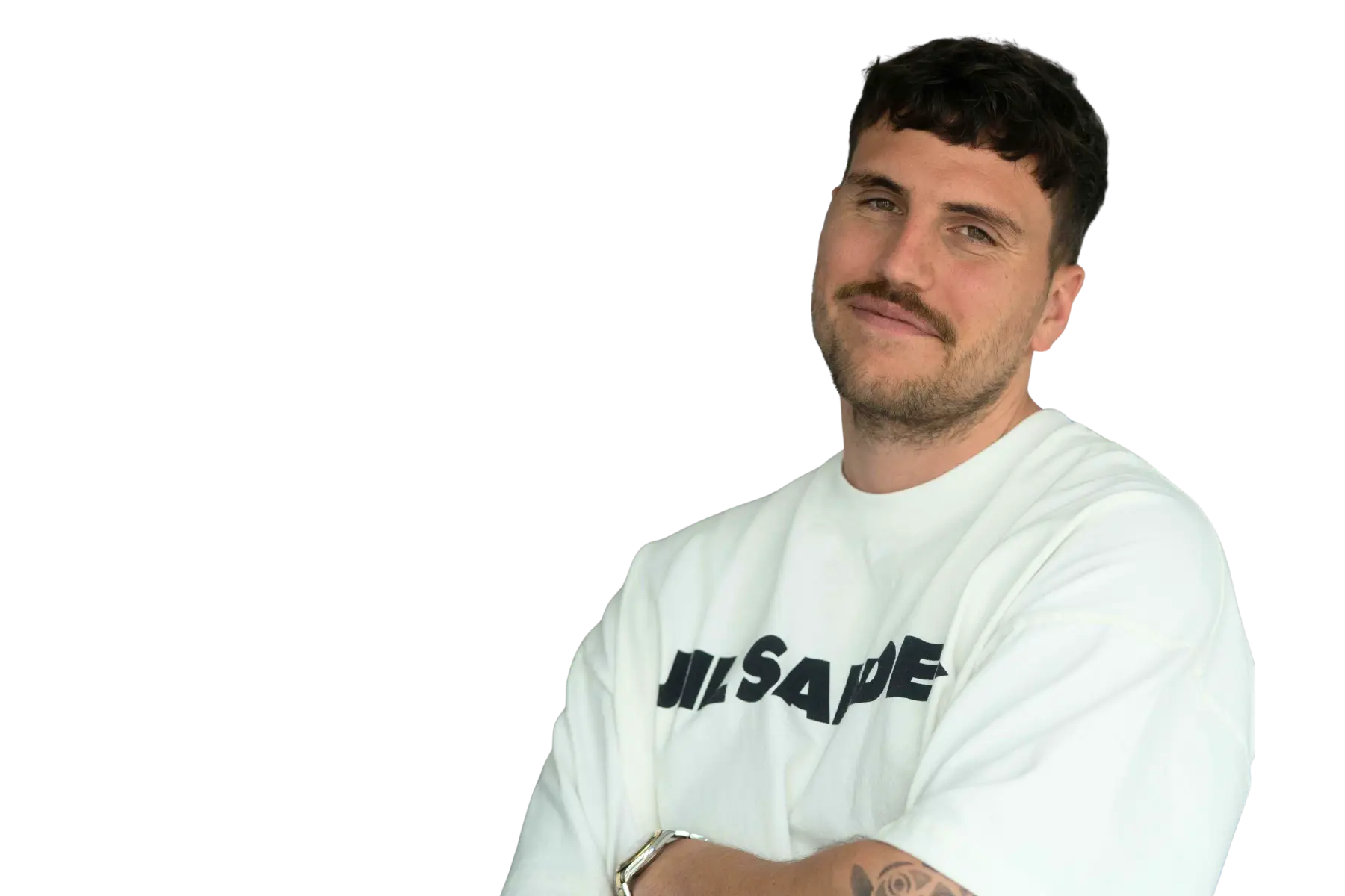 Porträt-Freisteller von Niclas Kroll mit kurzen, dunklen Haaren und Schnurrbart, lächelnd in einem weißen Jil Sander T-Shirt vor weißem Hintergrund.